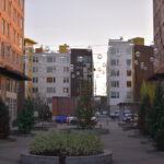 Exterior shot of Plaza Roberto Maestas, developed and owned by El Centro de la Raza. In the center is a courtyard with greenery and the sun is setting.