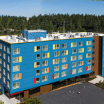 An aerial shot of an apartment building. The exterior color is teal, with yellow, red, and orange boxes as accents next to the windows. The building is six stories tall.