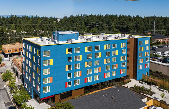 An aerial shot of an apartment building. The exterior color is teal, with yellow, red, and orange boxes as accents next to the windows. The building is six stories tall.